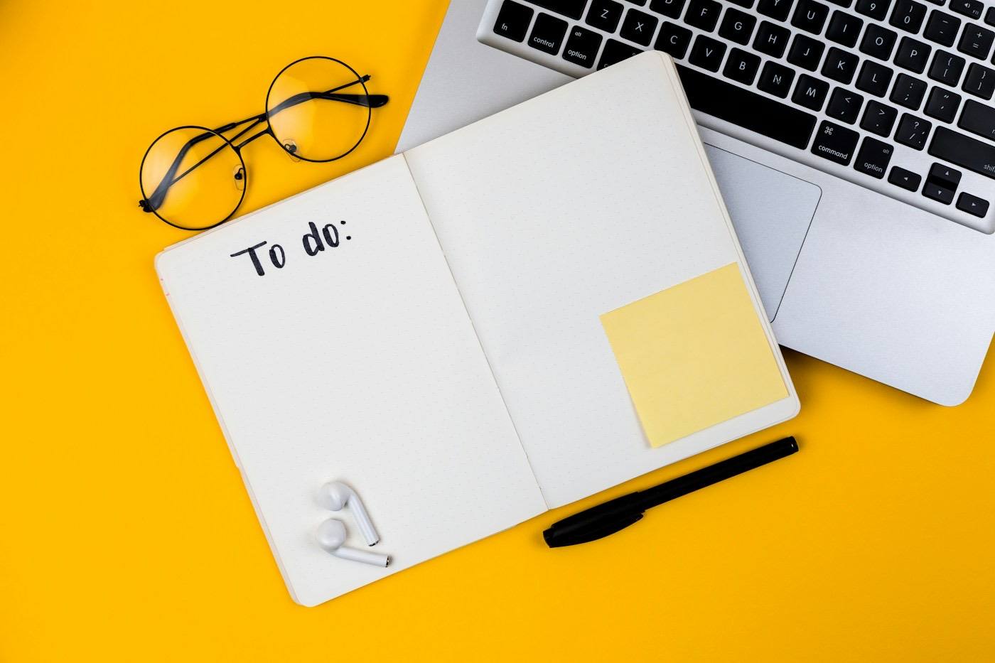 A laptop and notebook flat lay on a yellow desk